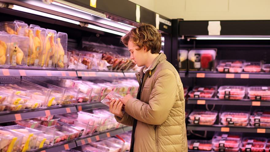 Junger Mann schaut sich Fleischverpackung im einem Supermarkt an