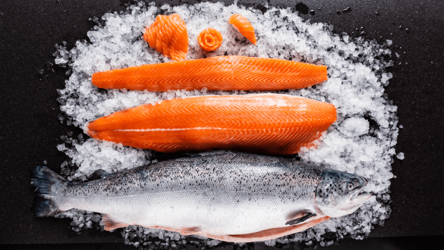 Ein Lachs und mehrere Lachsfilets liegen auf Eis.