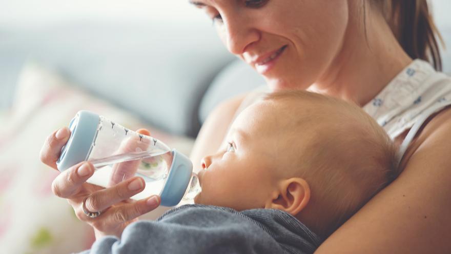 Frau hält einem Baby eine Trinkflasche mit Wasser an den Mund