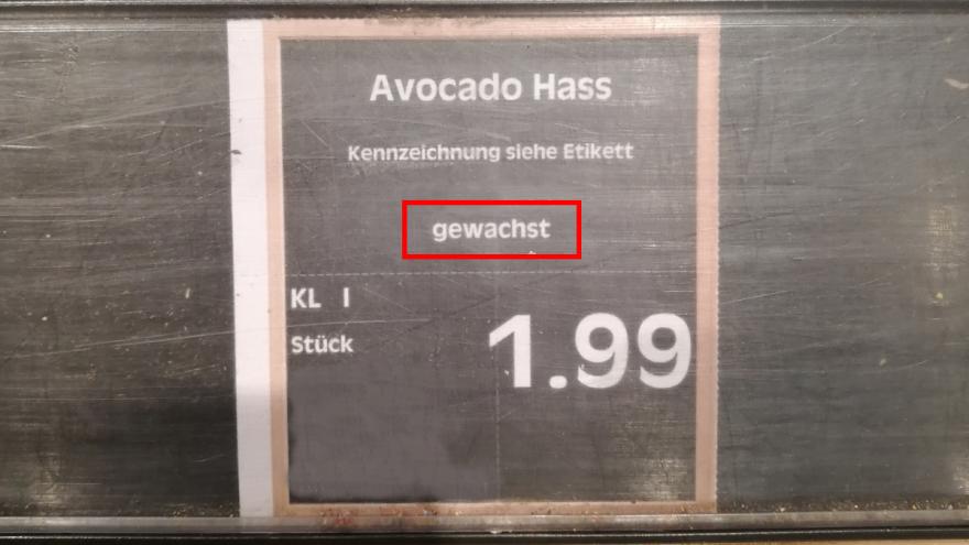 Preisschild für Avocado am Regal eines Supermarktes, auf dem gewachst steht 