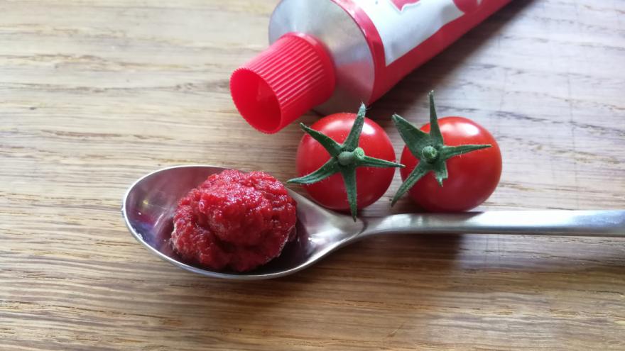 Ein Löffel Tomatenmark mit einer Tube und zwei Tomaten