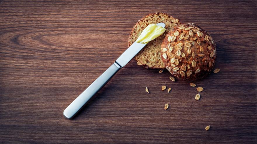 Auf einem Tisch liegt ein Mehrkornbrötchen und ein Messer mit Butter