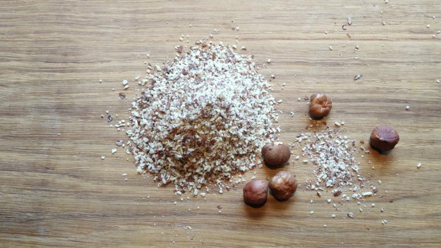 Ein Häufchen gemahlene Haselnüsse auf einem Holzbrett mit 5 Haselnüssen