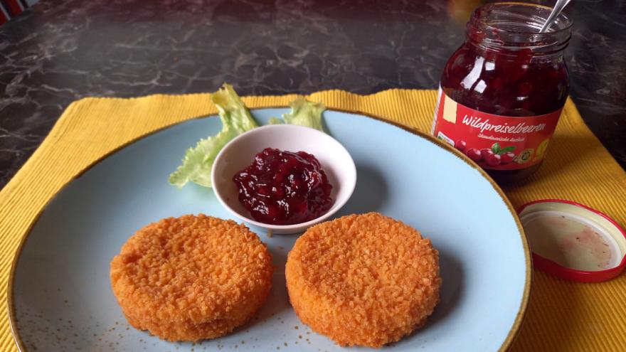 zwei Backcamembert auf einem Teller angerichtet mit Wildpreiselbeeren; daneben steht ein geöffnetes Glas Preiselbeeren