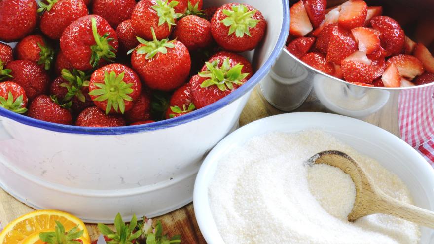 Viele Erdbeeren neben Töpfen, Zucker und weiteren Küchenuntensilien.