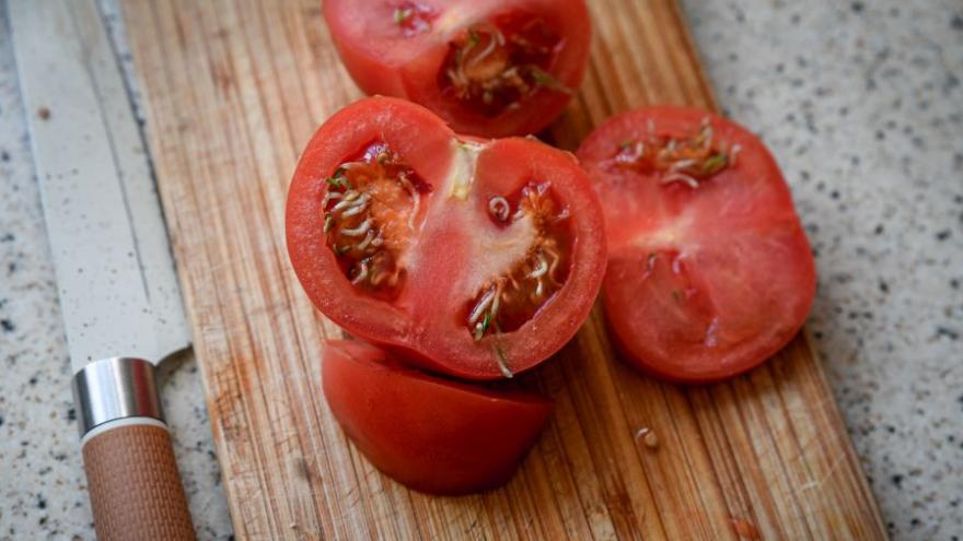 Foto von aufgeschnittenen Tomaten, die bereits keimen, auf einem Holzbrett. Daneben liegt ein Messer.
