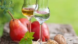 Ein Glas mit Birnenbrand vor Birnen.