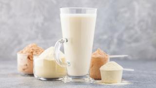 Ein Proteinshake im Glas steht neben einigen Pulvern auf dem Tisch.