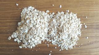 Grobe und feine Haferflocken liegen nebeneinander auf einem Holztisch.